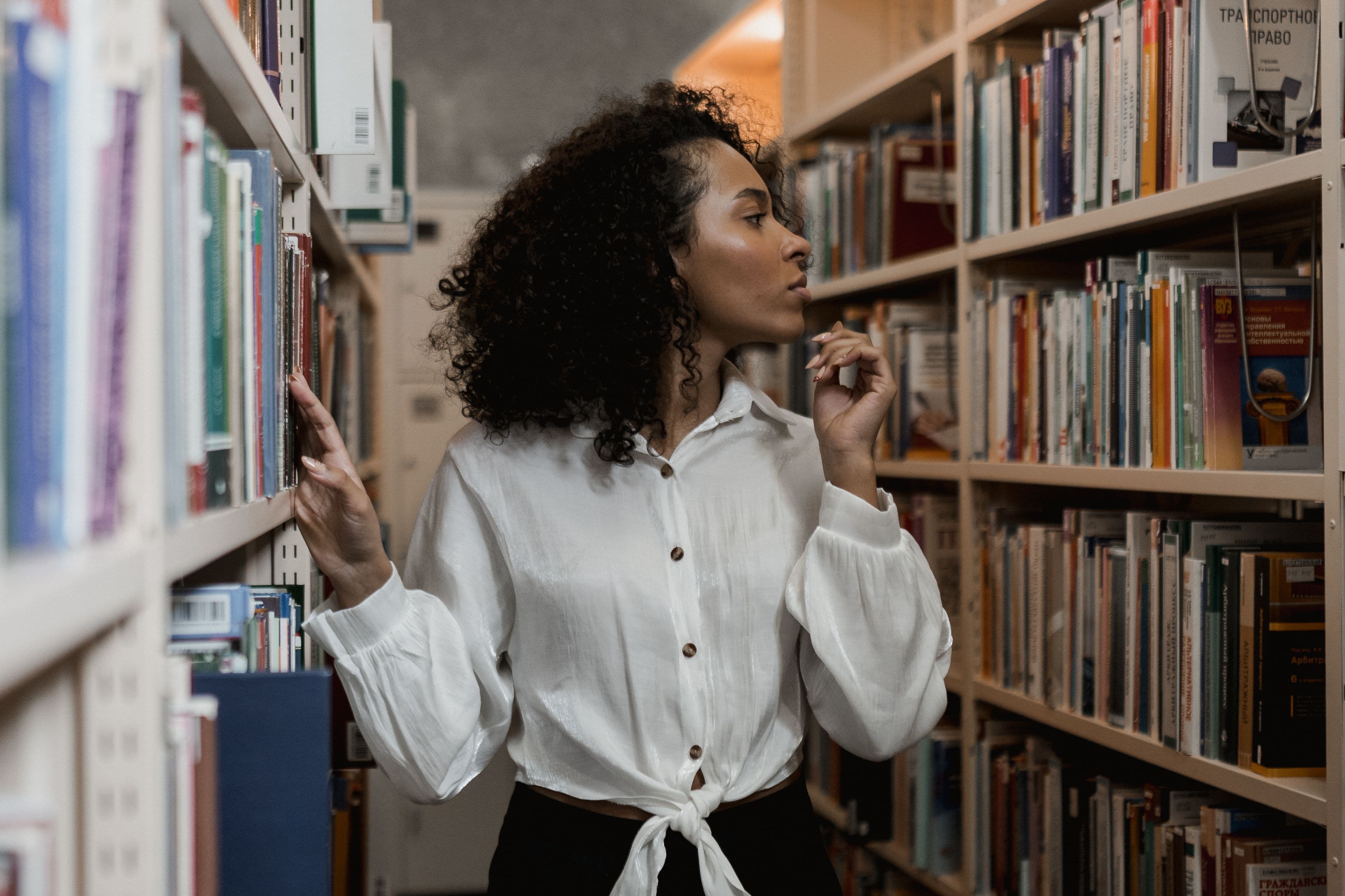 Curly-haired woman browsing bookshelves in a library