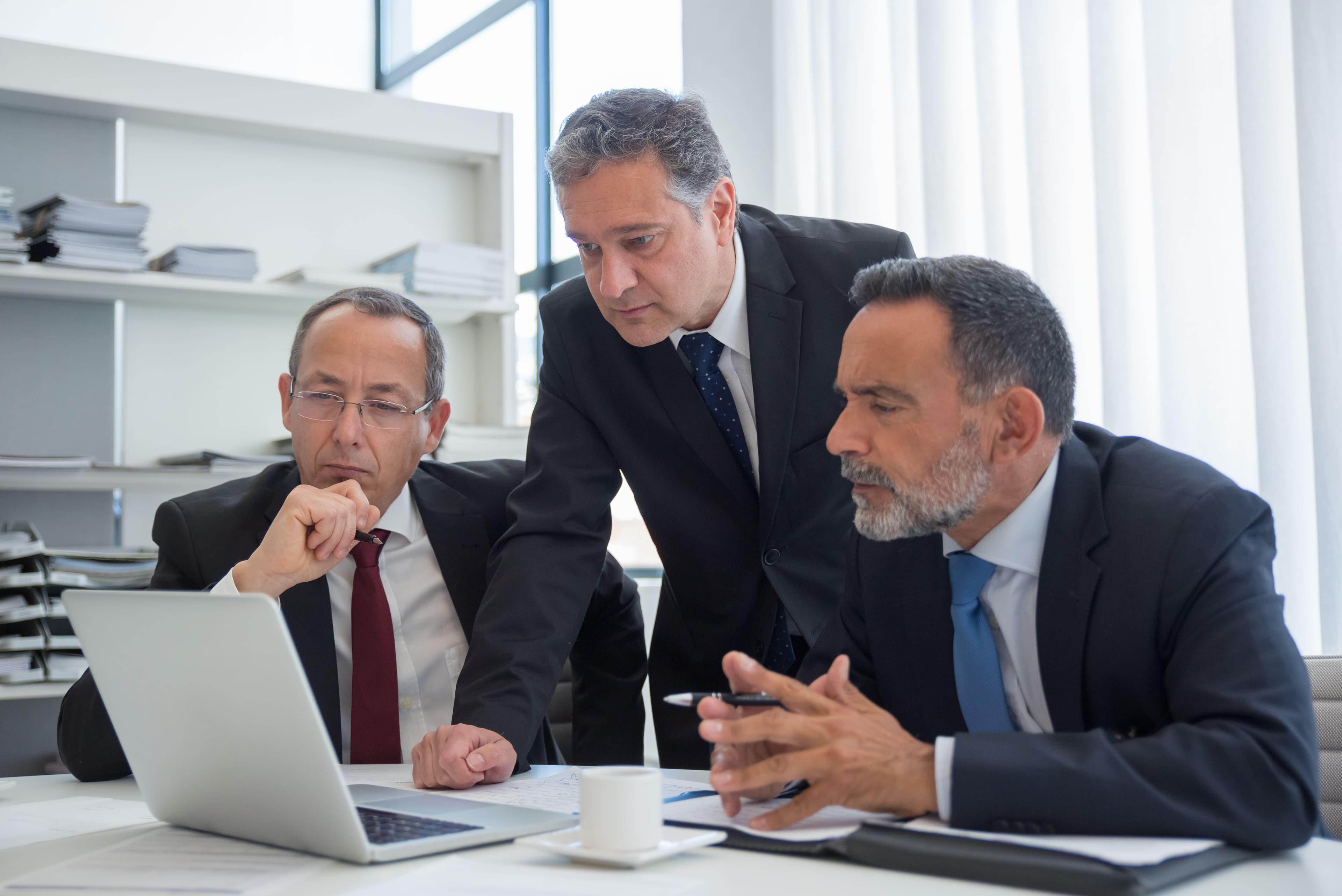Three businessmen in suits collaborating in a modern office setting