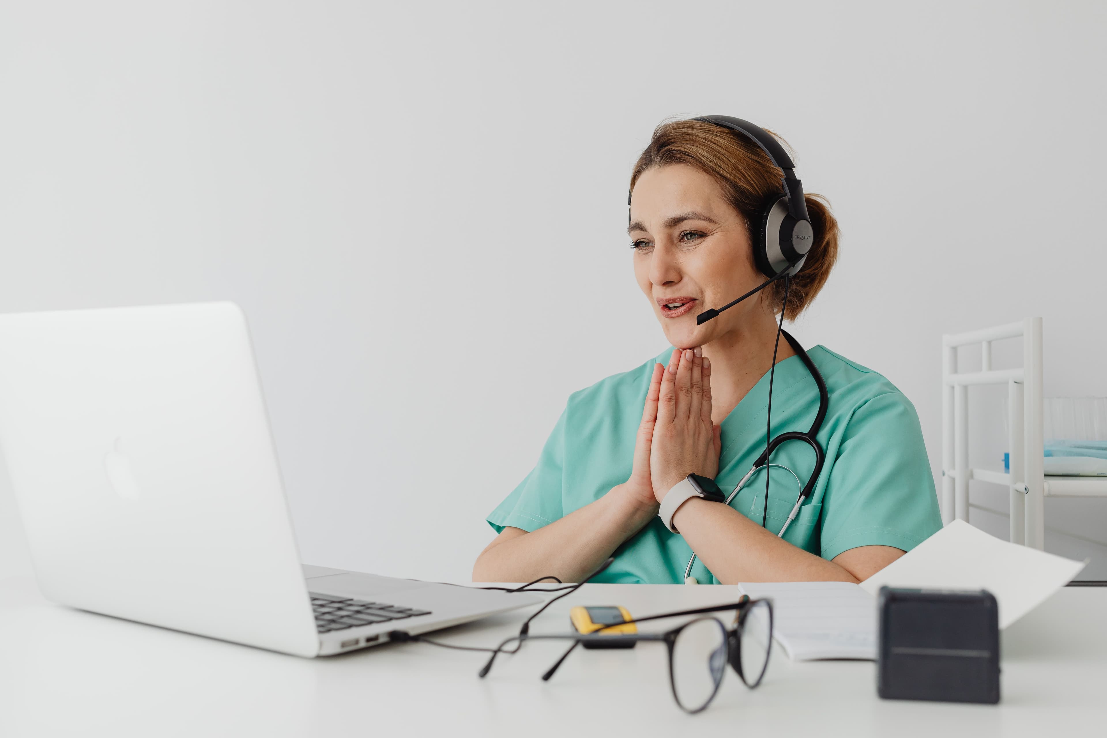 Female nurse using telemedicine for a virtual consultation on a laptop, wearing headphones and stethoscope