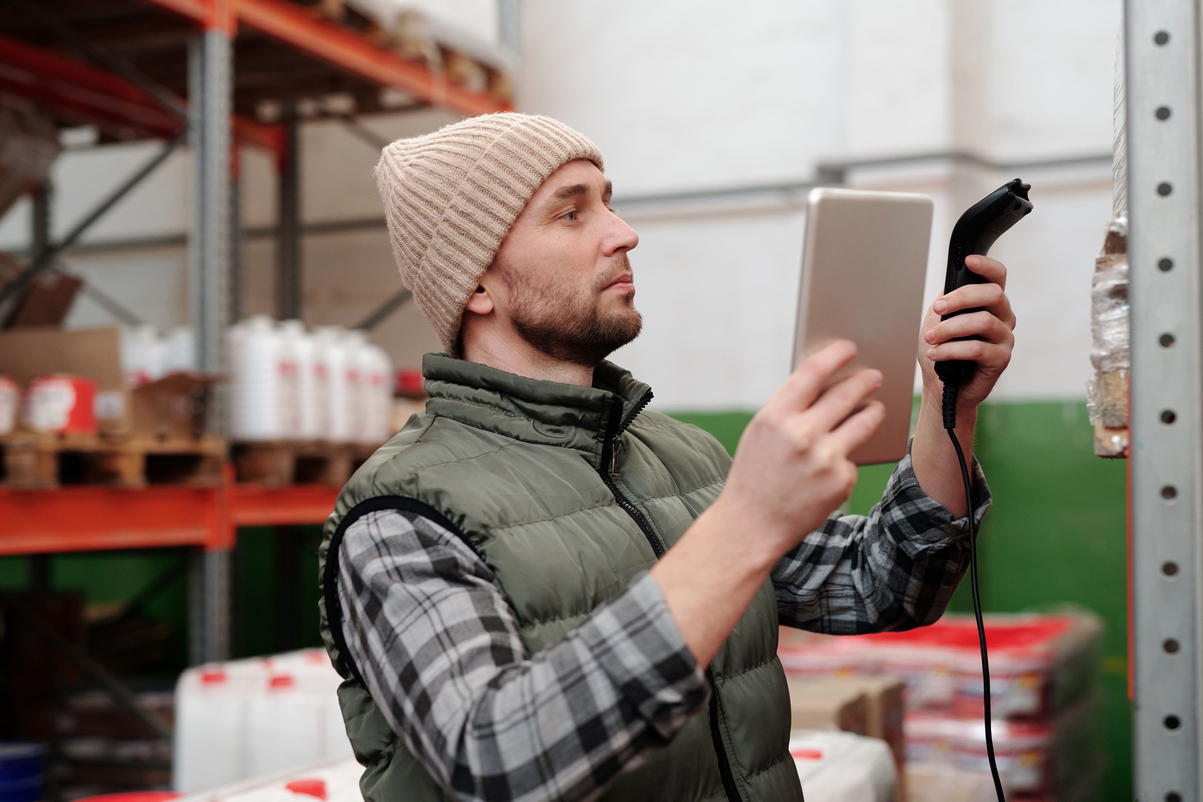 Man in beanie and vest using a scanner in a warehouse for inventory control