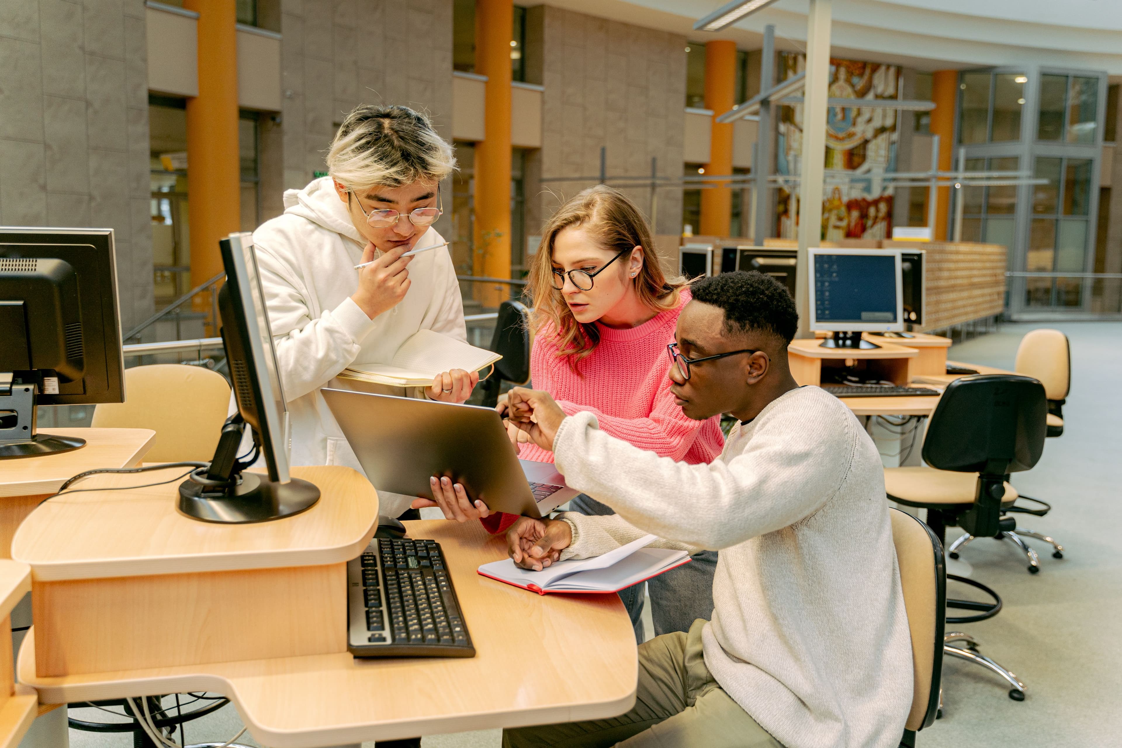 A group of students working on a laptop together in a modern library setting