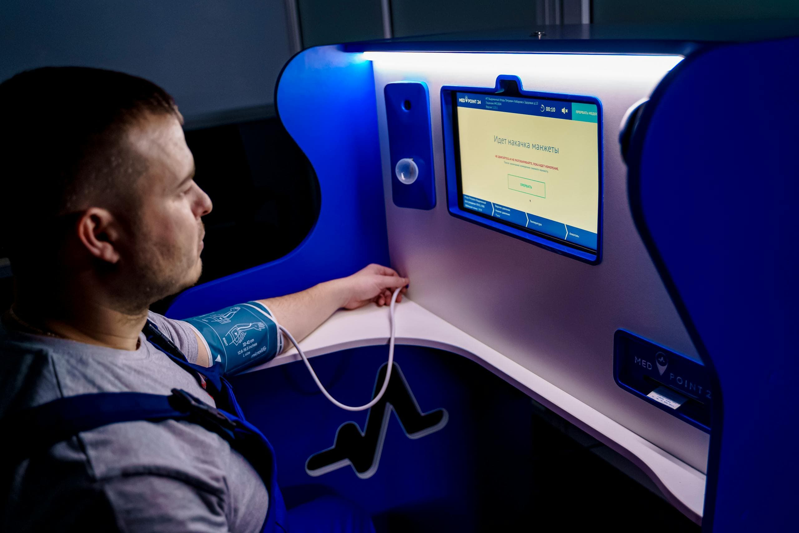 Man measuring blood pressure with a digital monitor at a self-service kiosk for telemedicine