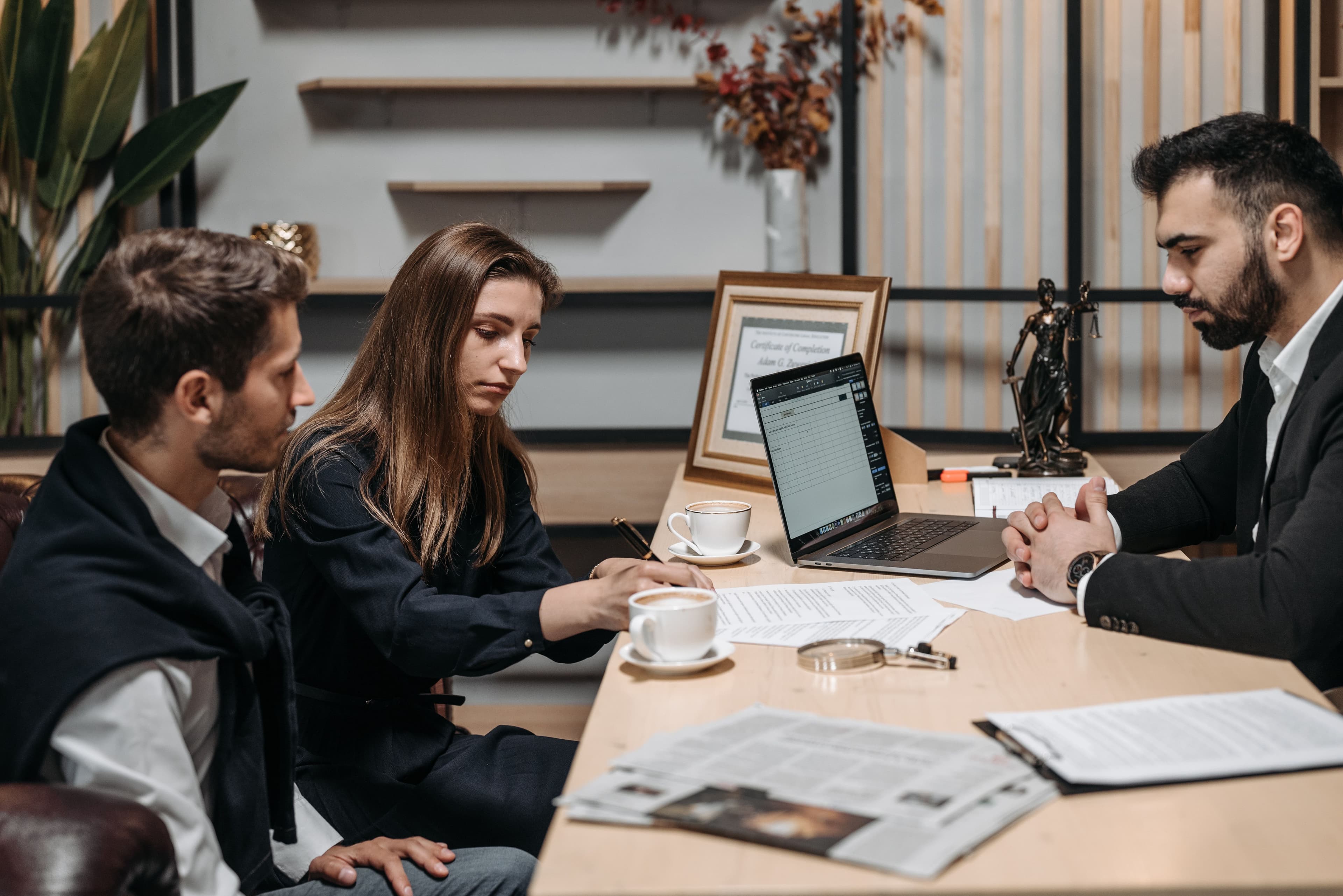 Three professionals discussing documents over coffee in a modern office setting