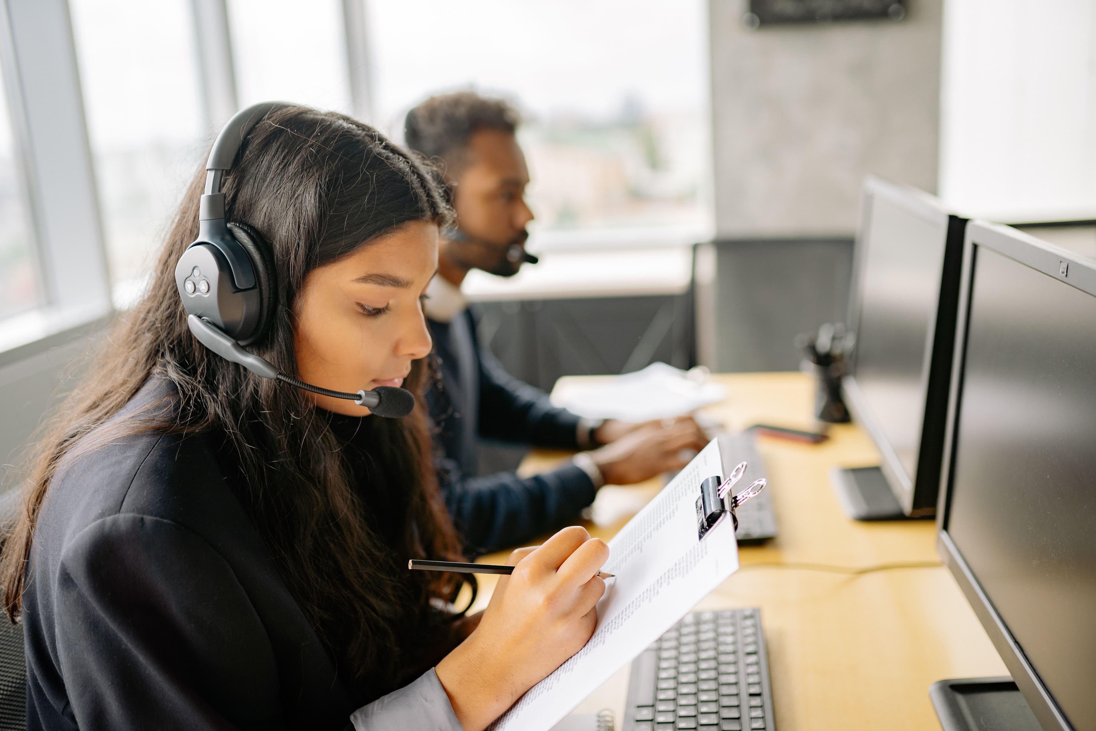 Two call center agents wearing headsets working at desks with computers in a modern office