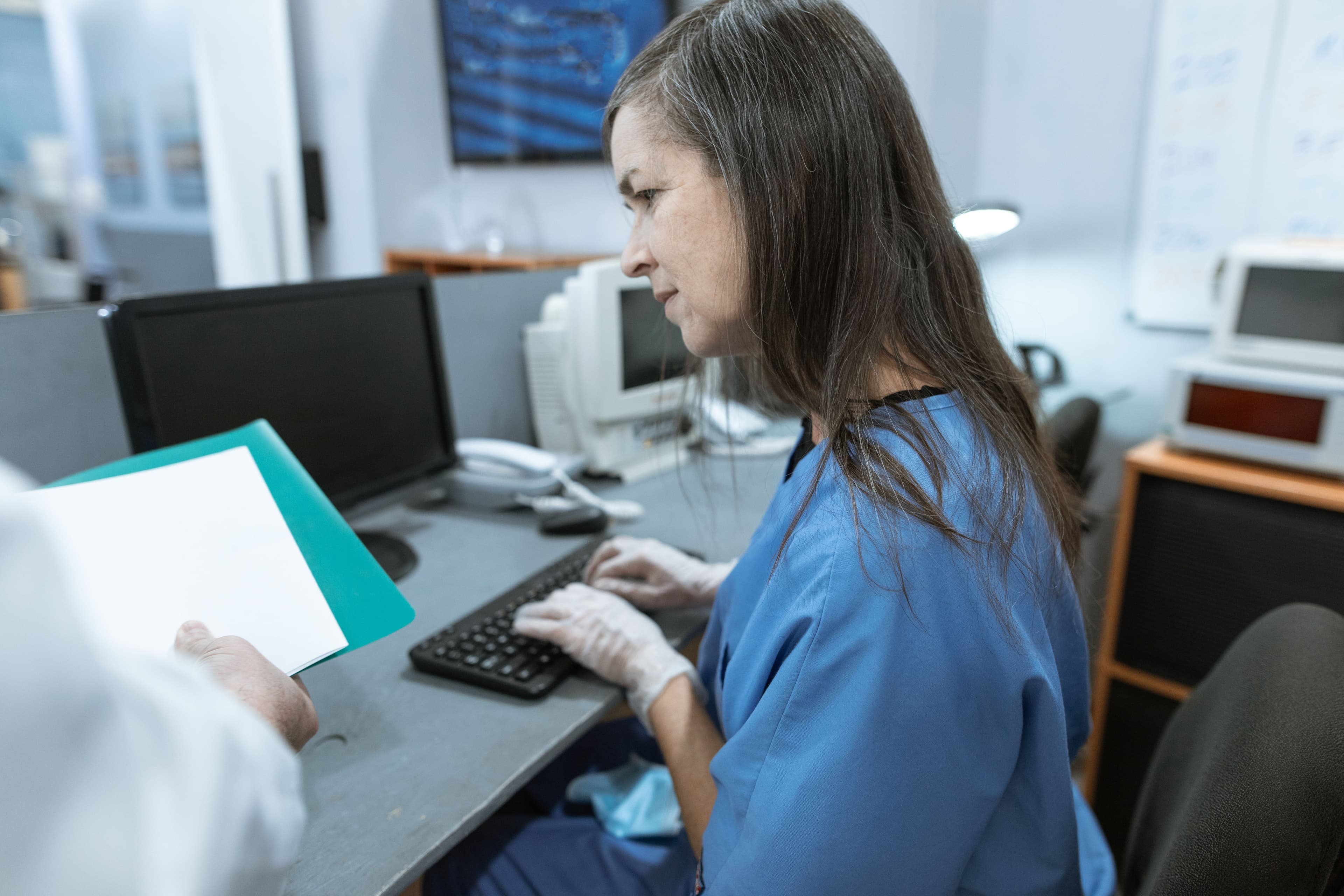 Nurse in scrubs typing on a keyboard at a medical workstation