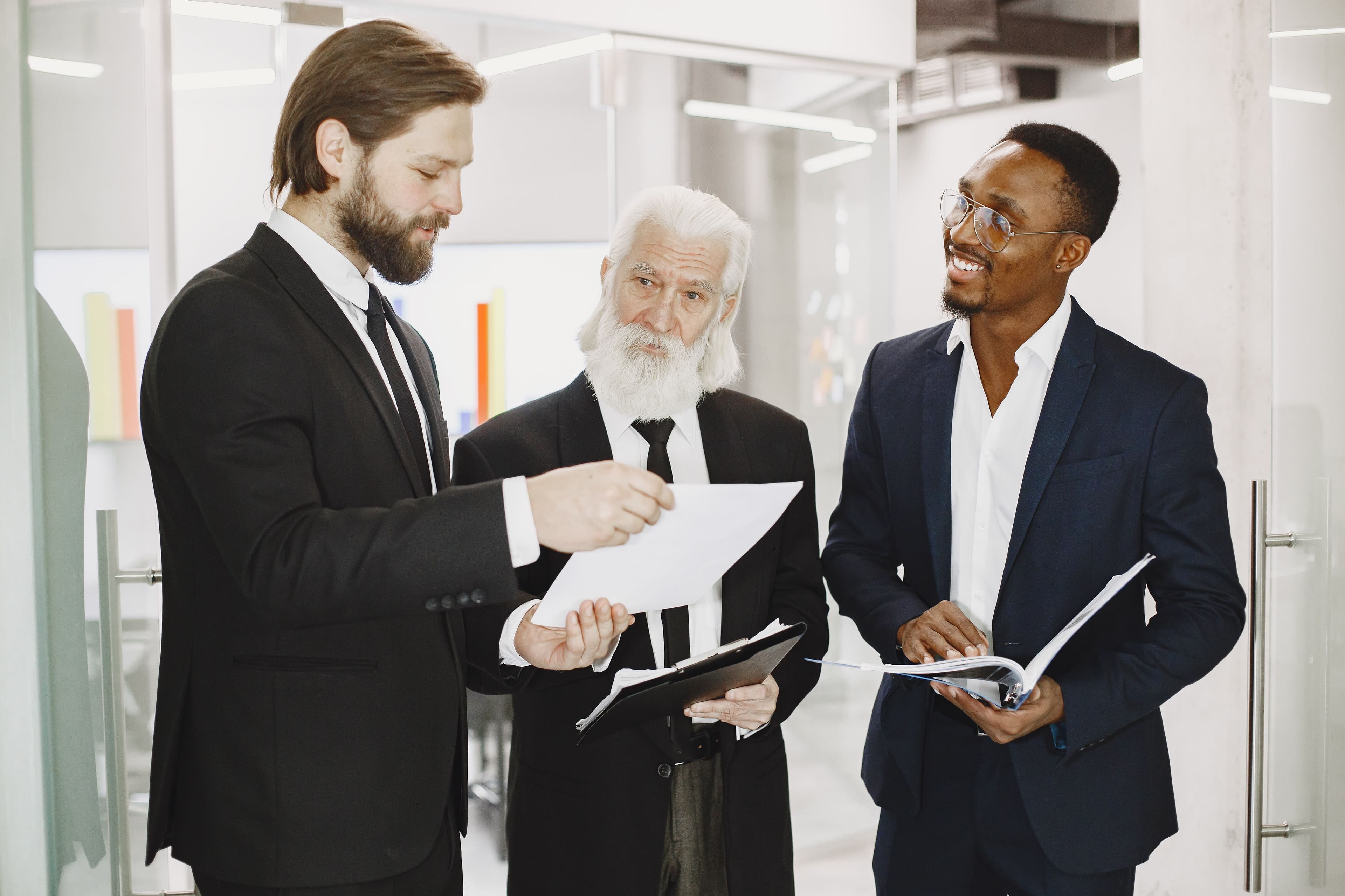 Three businessmen in suits discussing documents in a modern office setting, engaging in teamwork