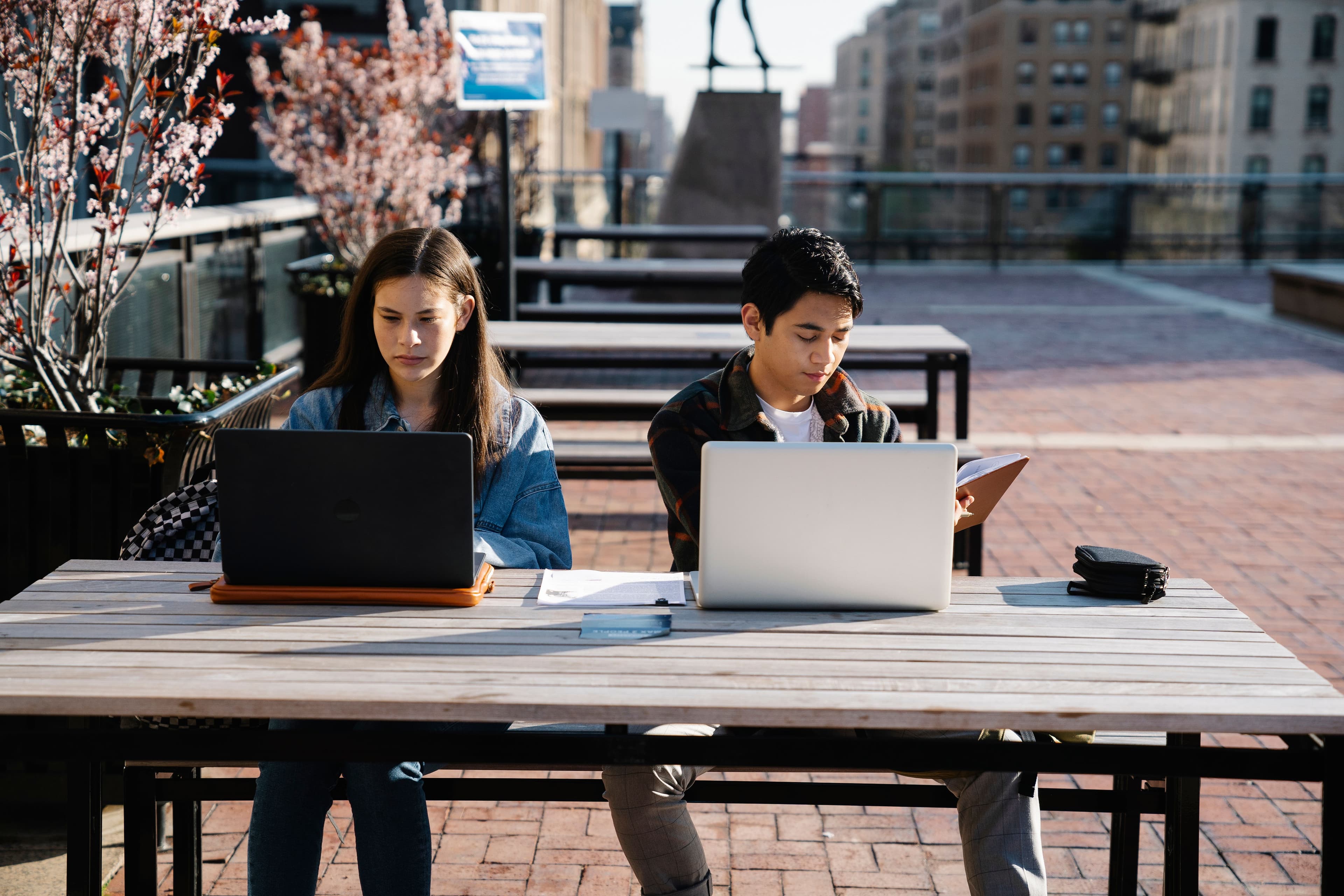 Young adults working on laptops outdoors at a table in a city setting