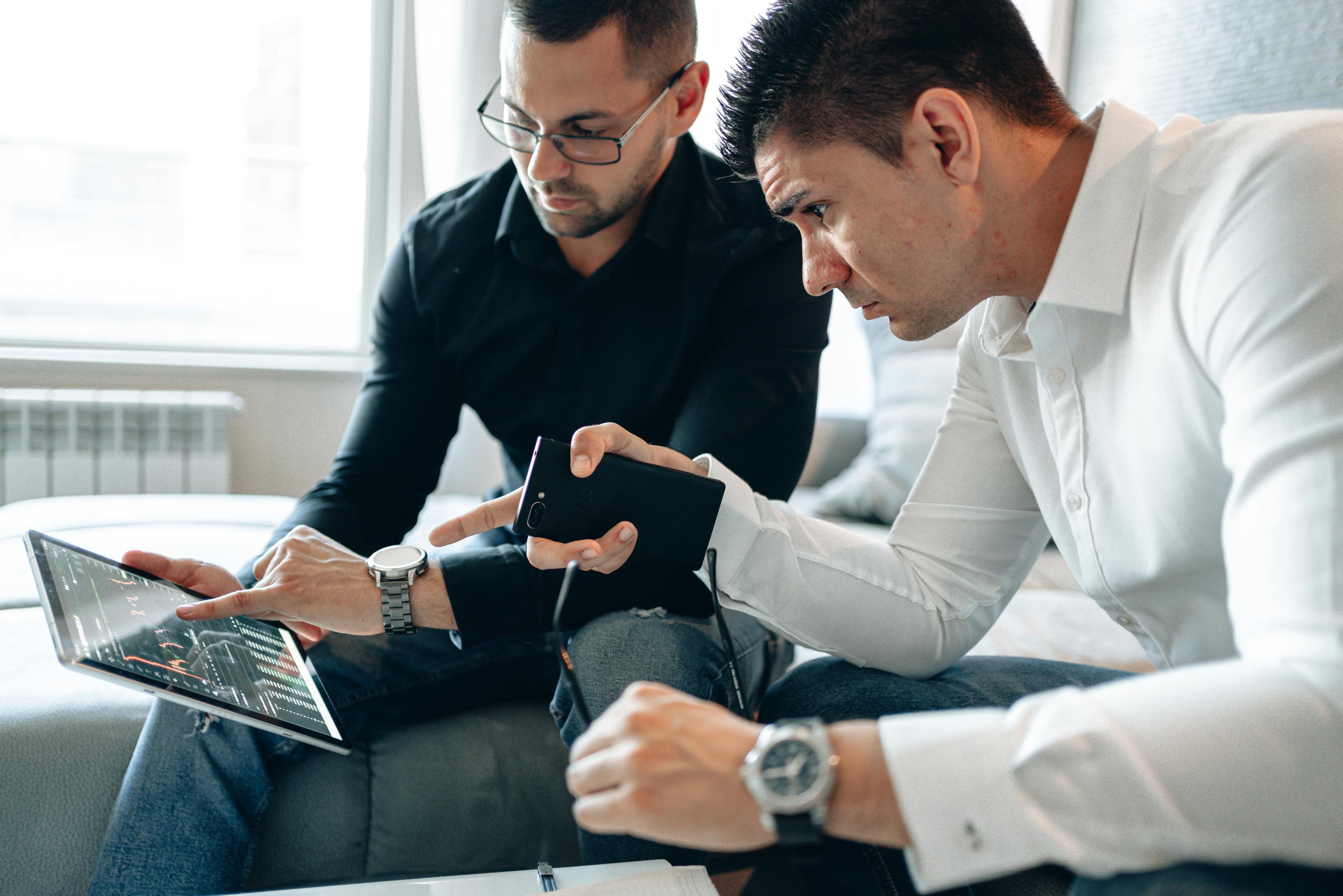 Two men analyzing financial data on a digital tablet indoors in a professional setting