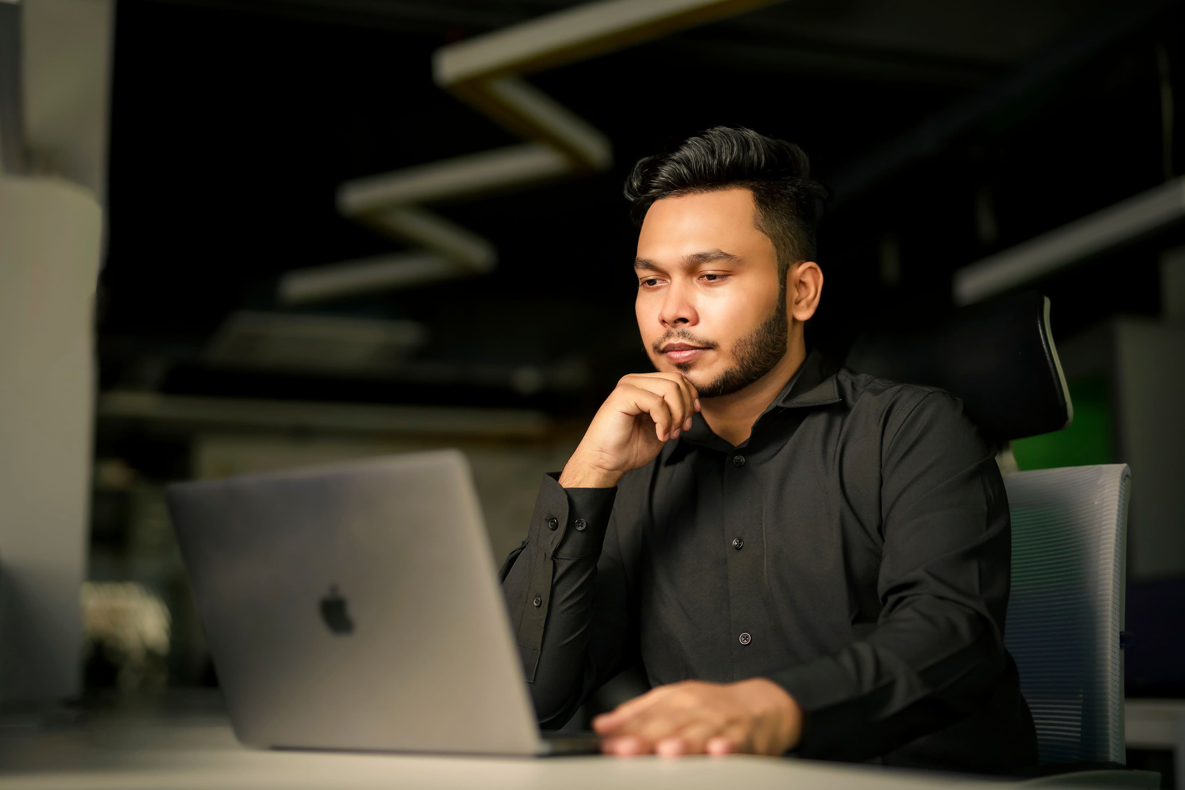 Man in black shirt concentrating on work with laptop in modern office